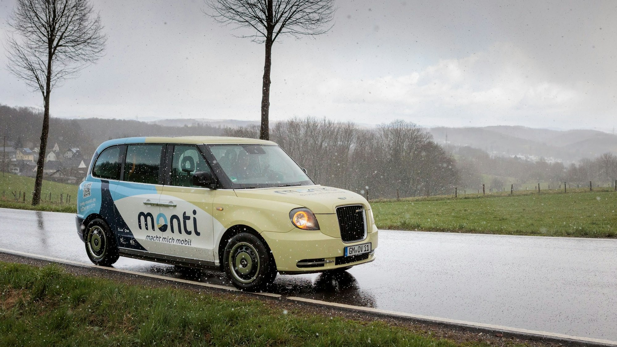 Ein eierschalenfarbenes Auto fährt auf einer verregneten Straße.