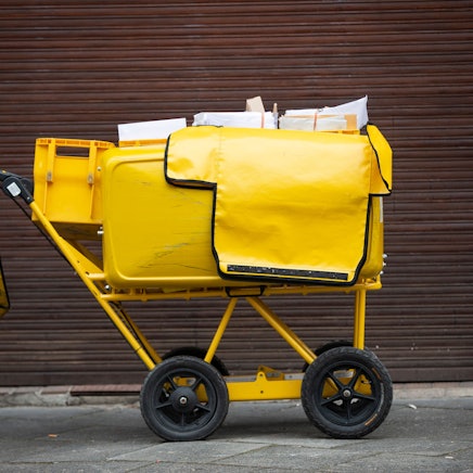Ein Briefträgerwagen der Deutschen Post für die Hausbelieferung steht auf einer Straße.