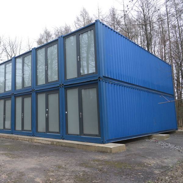 Blaue Unterkunft/Container für Geflüchtete Flüchtlinge in Odenthal stehen auf einem Parkplatz am Wald.