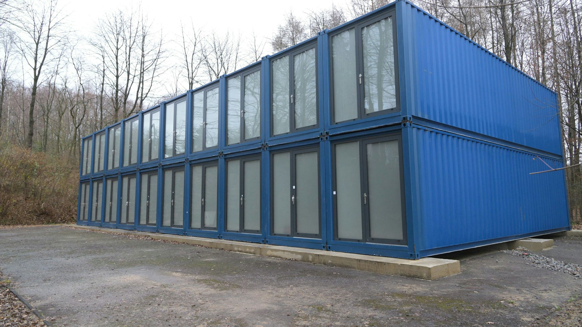 Eine Reihe von blauen Containern mit großen Glastüren, in zwei Etagen aufeinandergestapelt.