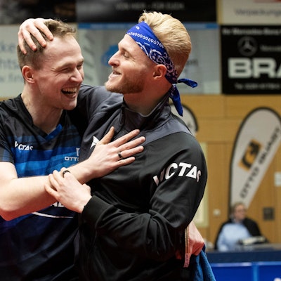 Zwei Tischtennisspieler liegen sich lachend in den Armen.