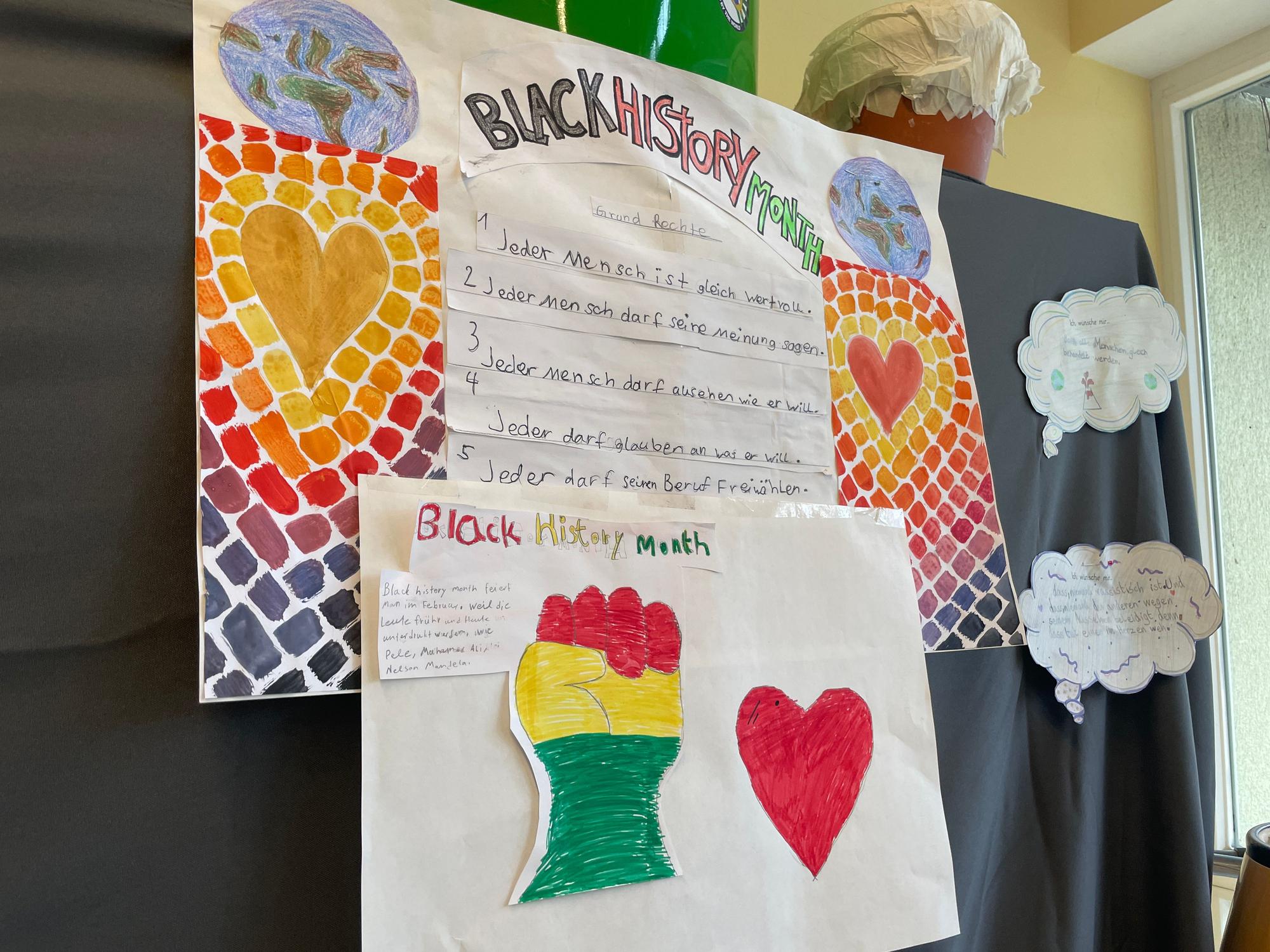 Auf einem bunten Poster steht das Grundgesetz in Handschrift geschrieben. Darüber und darunter steht „Black History Month“ geschrieben.