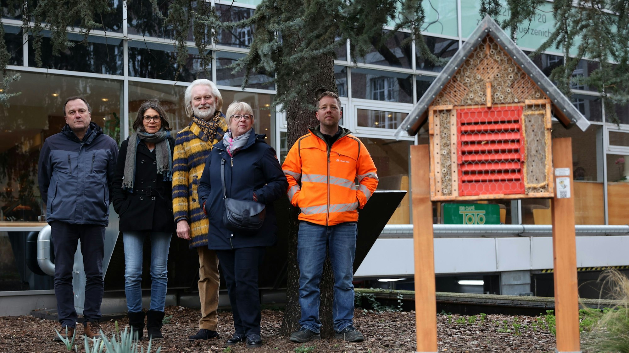 Fünf Menschen stehen links neben einem Bienenhotel.