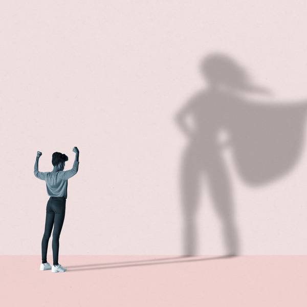 Eine junge Frau streckt ihre Arme in die Höhe, vor einer rosafarbenen Wand, auf der der Schatten einer Superwoman erscheint.