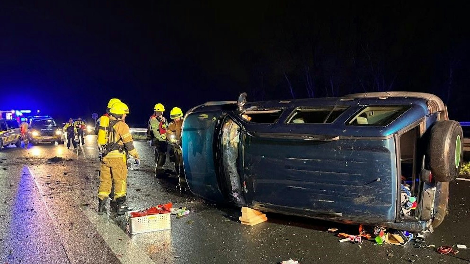 Feuerwehrleute stehen an dem verunglücktem Auto. Auf der Fahrbahn liegen Trümmerteile.