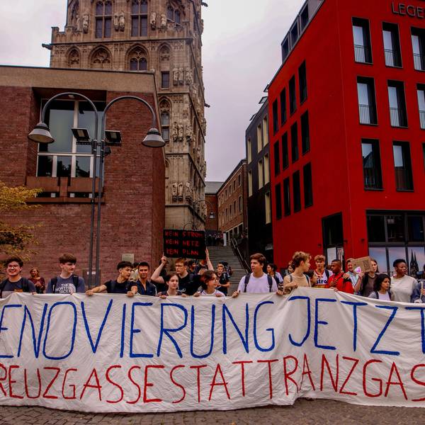 Schüler und Eltern des Gymnasiums Kreuzgasse demonstrieren im Sommer 2022 für eine Sanierung des Schulgebäudes vor dem Historischen Rathaus auf dem Alter Markt in Köln. Sie halten ein Transparent mit den Worten „Renovierung Jetzt! Kreuzgasse statt Ranzgasse“ hoch.