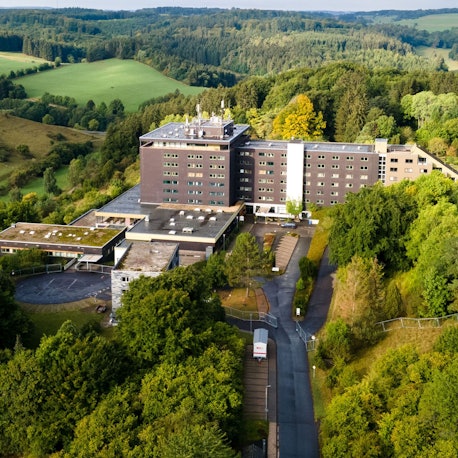 Das große Gebäude der früheren Eifelhöhen-Klinik in Marmagen, die jetzt als Unterkunft für Geflüchtete genutzt wird, liegt am Ortsrand von Marmagen und ist von idyllischer Natur umgeben.