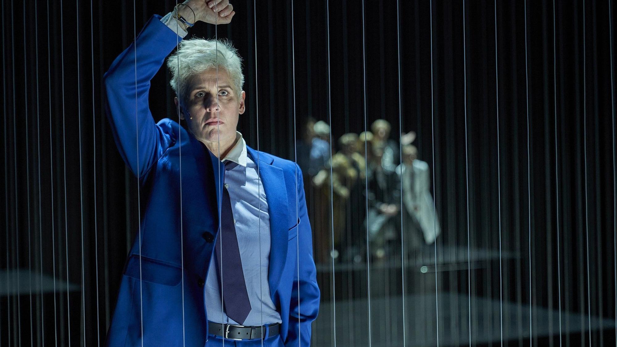 Die Schauspielerin Melanie Kretschmann lehnt sich in der Rolle des Johann Holtrop auf der Bühne des Depot 1 des Schauspiels Köln an ein Gitter aus Fäden.