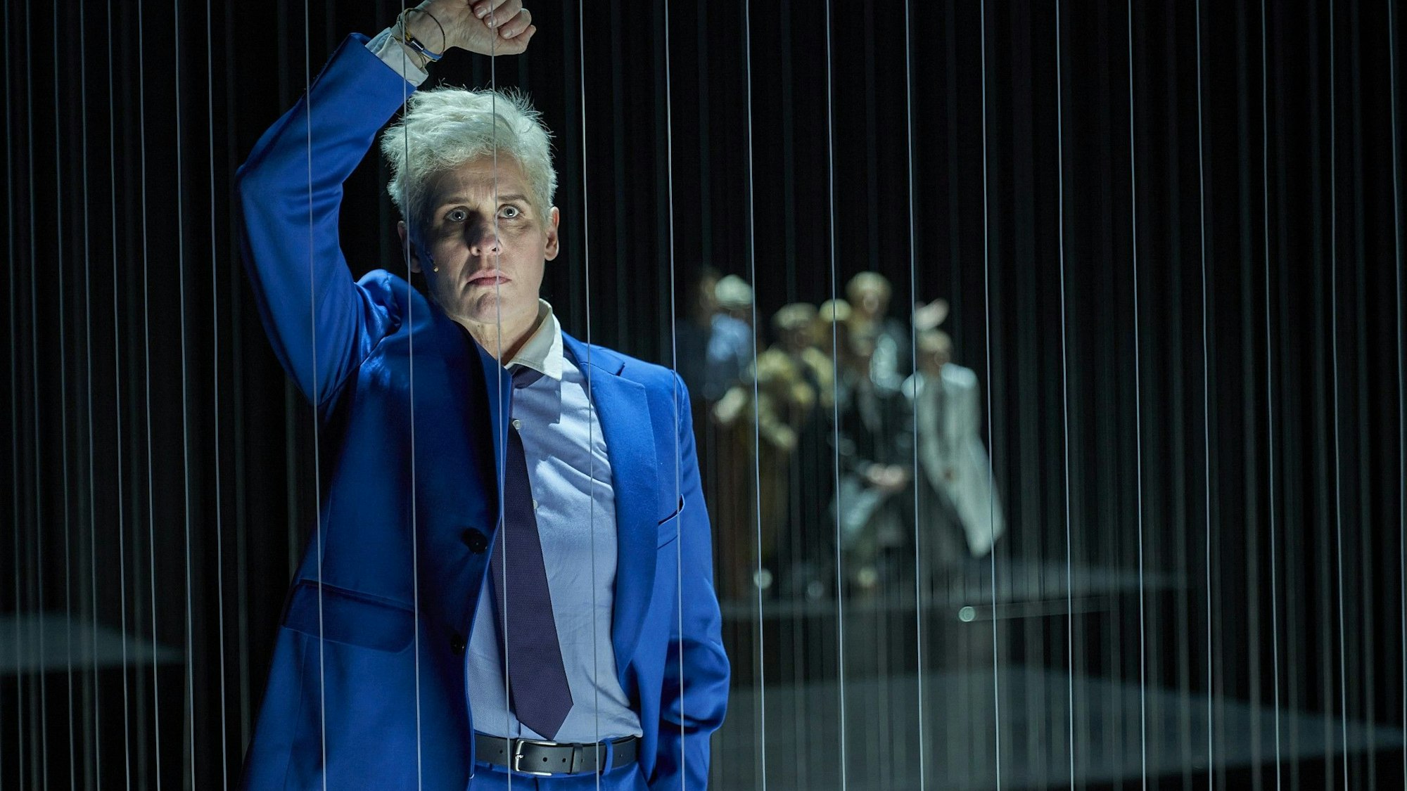 Die Schauspielerin Melanie Kretschmann lehnt sich in der Rolle des Johann Holtrop auf der Bühne des Depot 1 des Schauspiels Köln an ein Gitter aus Fäden.