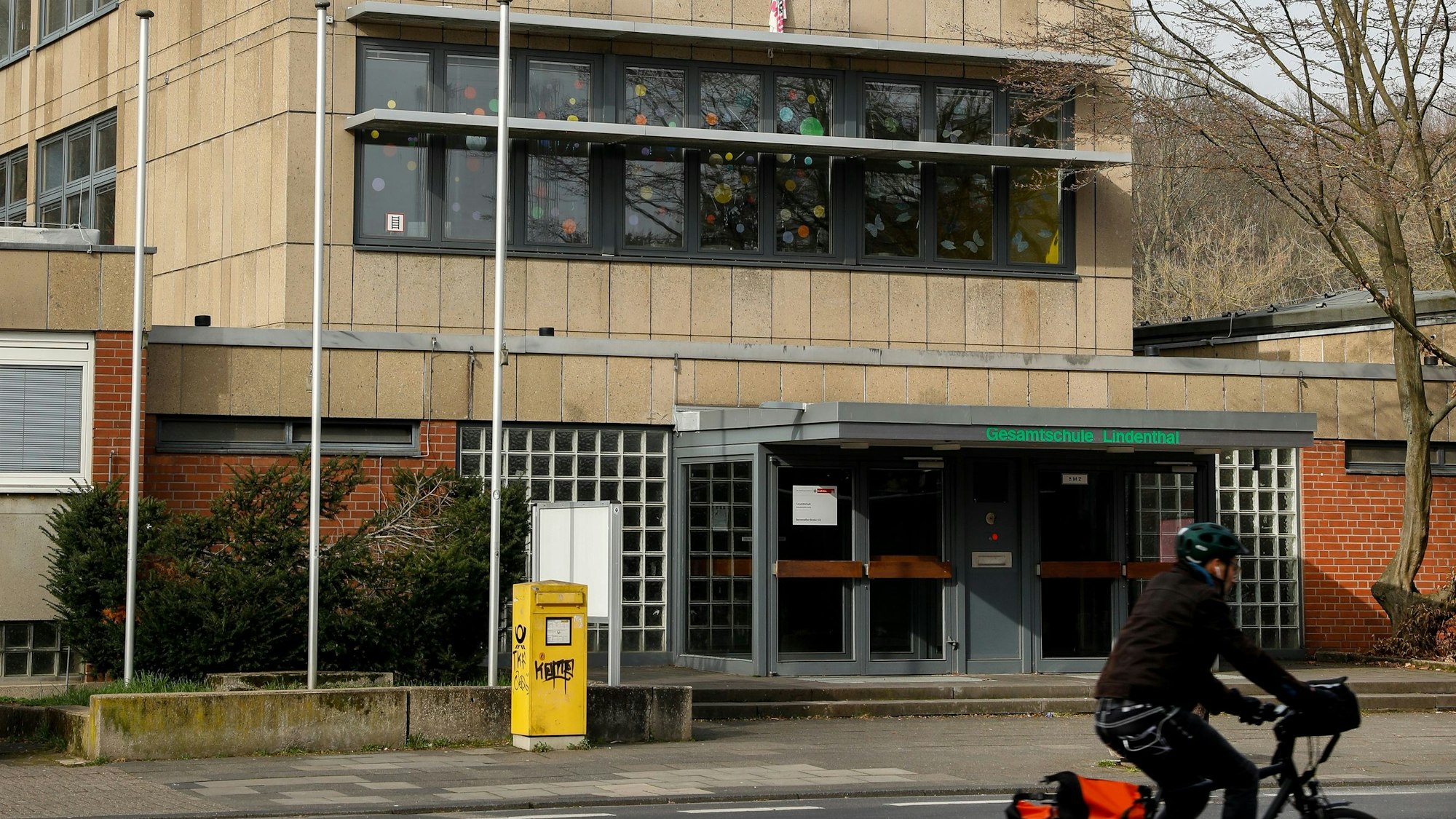 Man sieht den Eingang einer Schule, davor einen Briefkasten und ein Radfahrer.