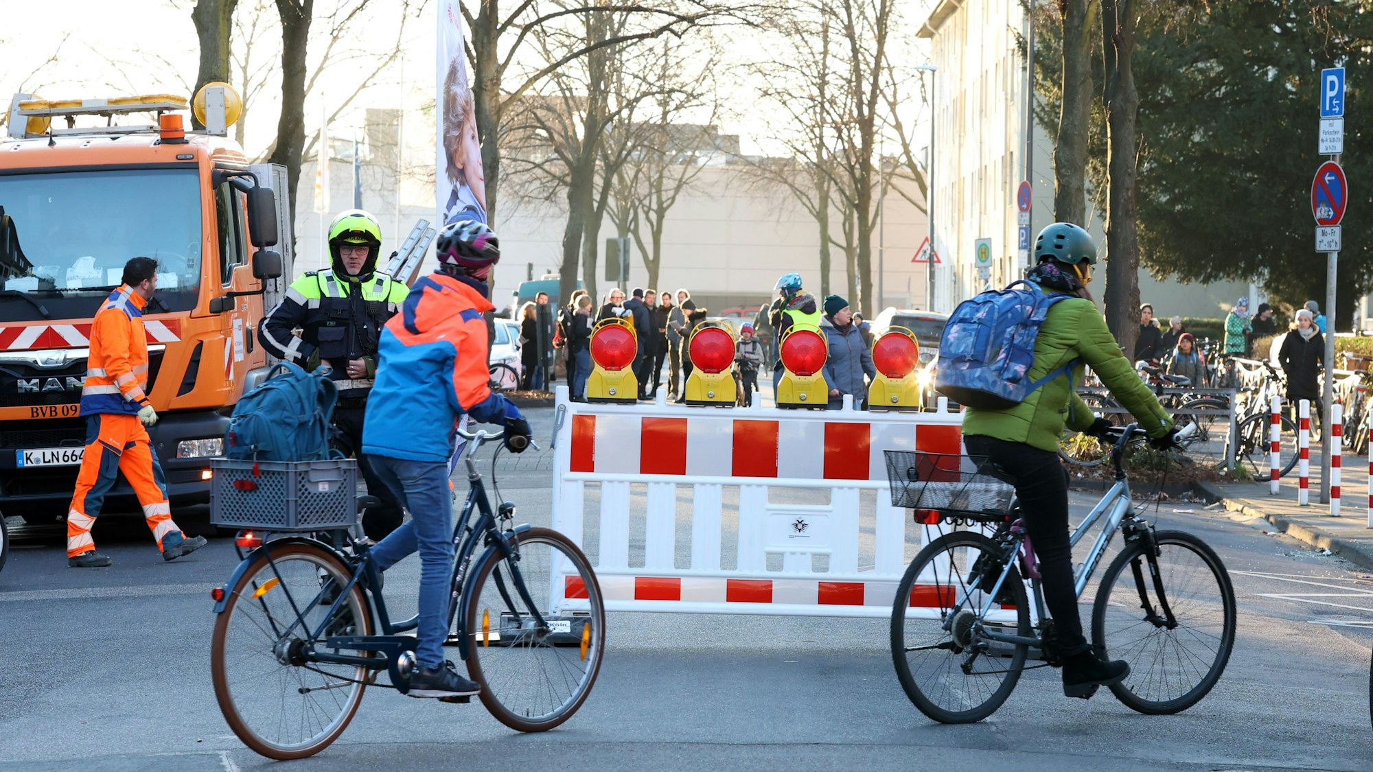 Zwei Kinder fahren mit dem Fahrrad über die Straße, die mit einer Bake für den Autoverkehr gesperrt ist.