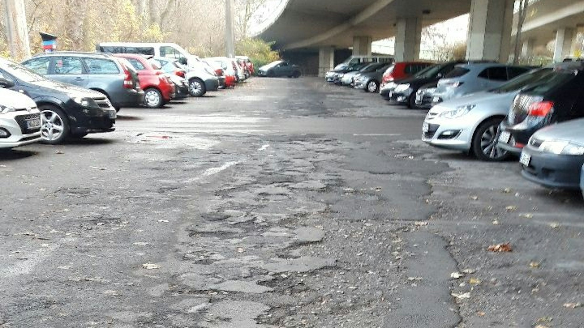 Kaputte Asphaltdecke mit parkenden Autos zu beiden Seiten