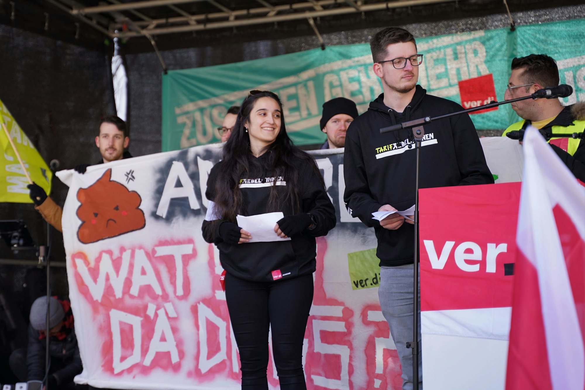 Betül und Florian von Verdi vor anderen Streikenden auf der Bühne.
