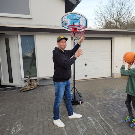 Nick Mertens steht mit seinem Vater in der Einfahrt und spielt Basketball.