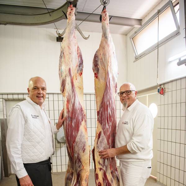 Zwei Männer stehen neben zwei aufgehängten Rinder-Vierteln.