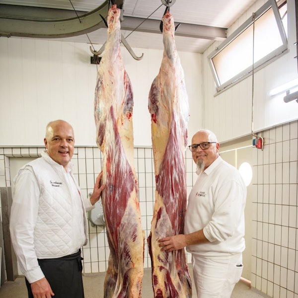 Zwei Männer stehen neben zwei aufgehängten Rinder-Vierteln.