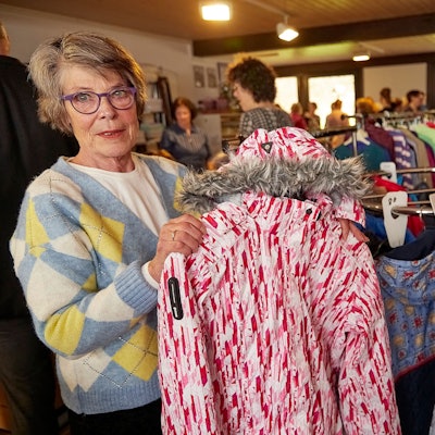 Leiterin Inge Wergen hält ein Kleidungsstück in der Hand. Im Hintergrund sieht man die Räumlichkeiten der neuen Kleiderkammer.