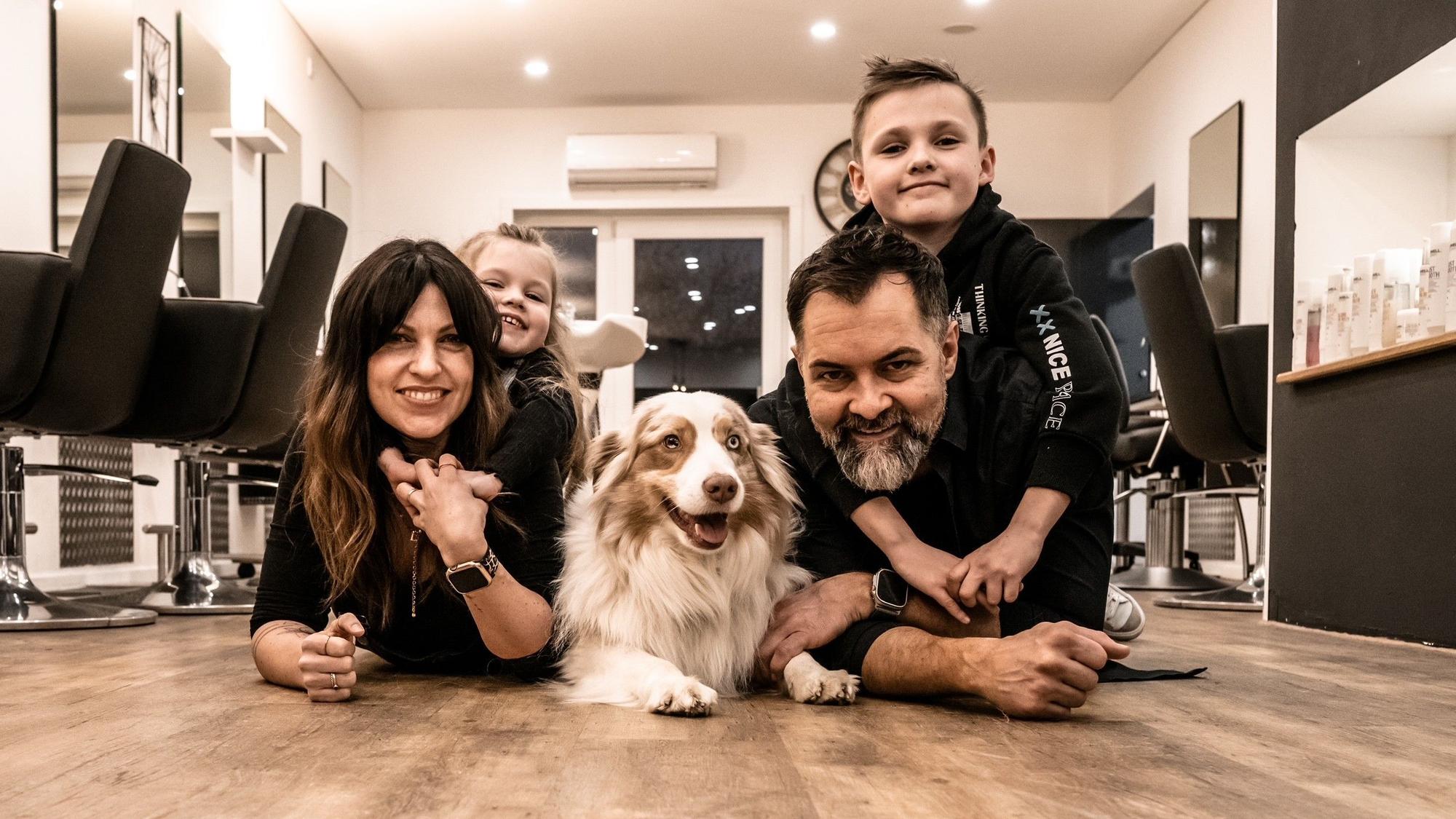 Friseur Salon von Daniel und Ela Gansäuer in Windeck Hurst mit den Kindern und dem Hund. Sie liegen auf dem Boden des Salons und lächeln die Kamera an.