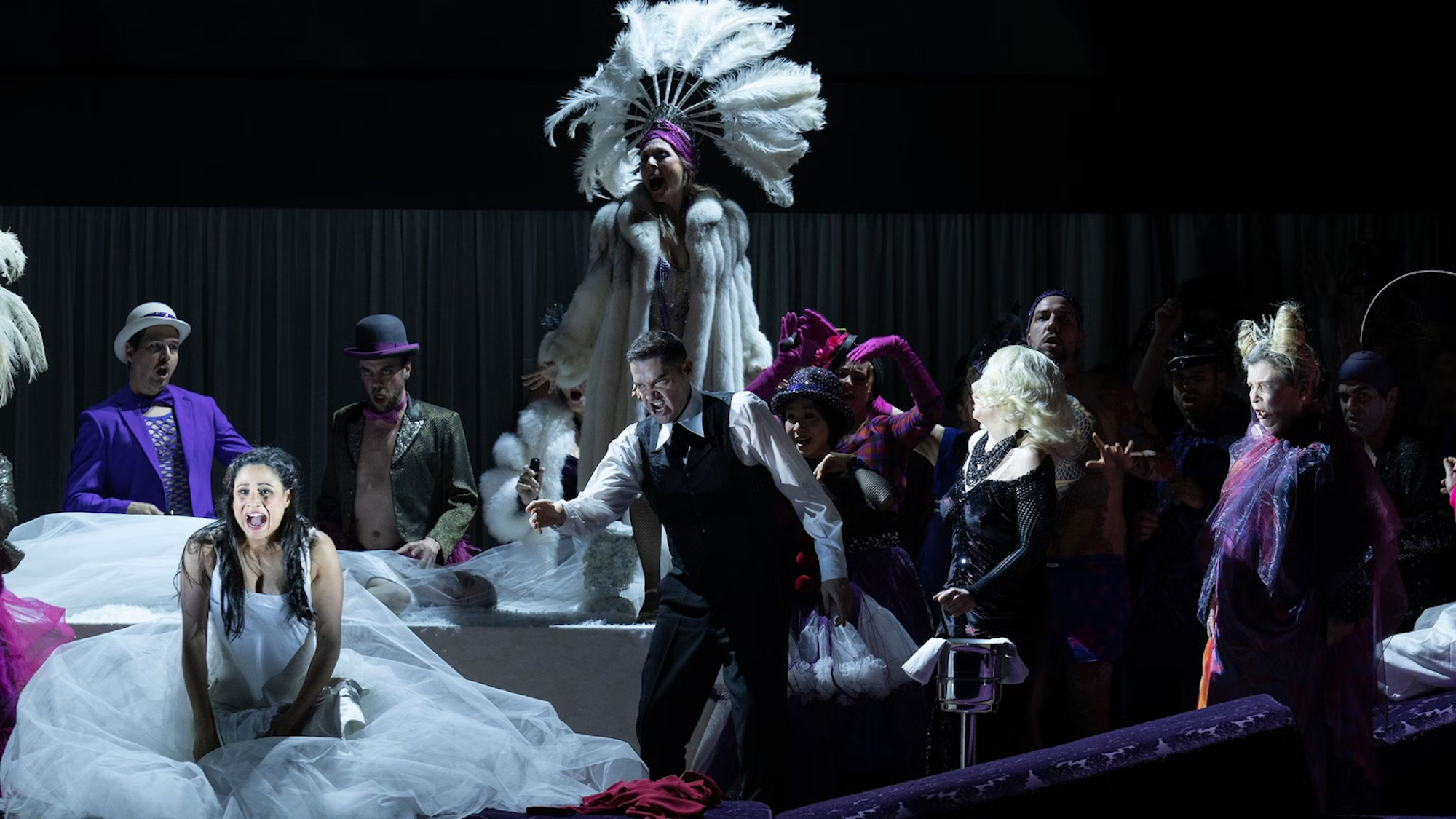 Eine schlafwandlerische Opernszene aus Bellinis „La Sonnambula“. Dämonen und lila gekleidete Herren umtreiben eine Frau im weißen Brautkleid.
