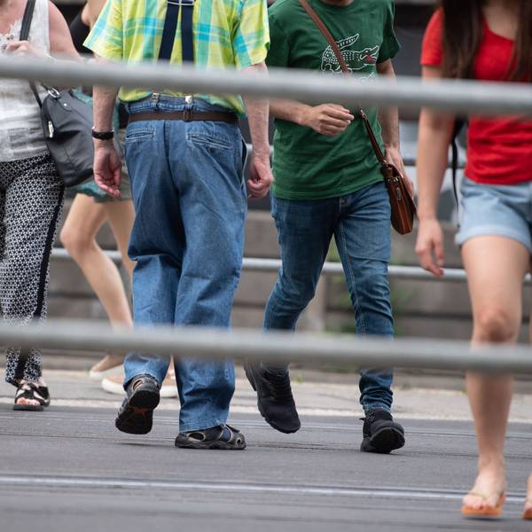 Es sind die Unterkörper mehrere Menschen zu sehen, die über die Straße laufen. Der Fokus des Bildes liegt auf dem Fußverkehr im Straßenverkehr.
