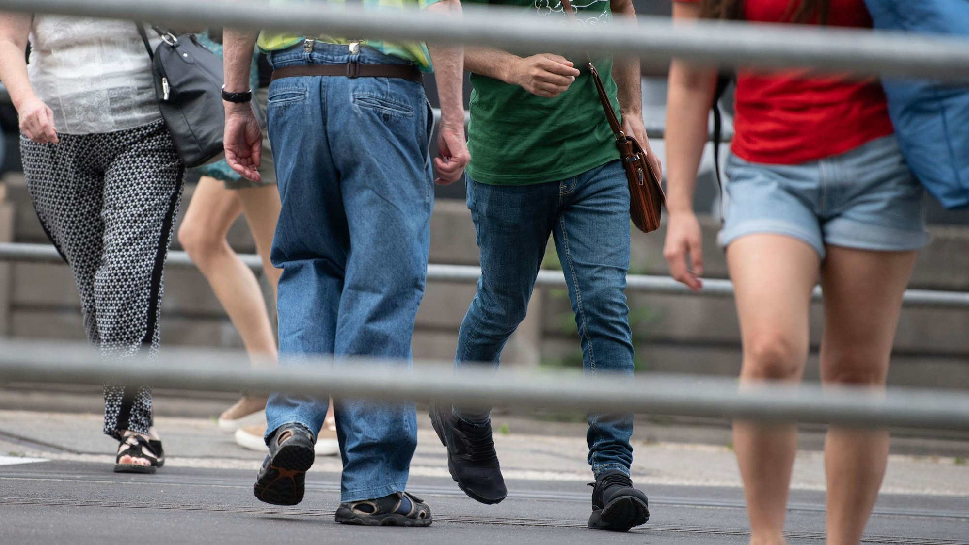 Es sind die Unterkörper mehrere Menschen zu sehen, die über die Straße laufen. Der Fokus des Bildes liegt auf dem Fußverkehr im Straßenverkehr.