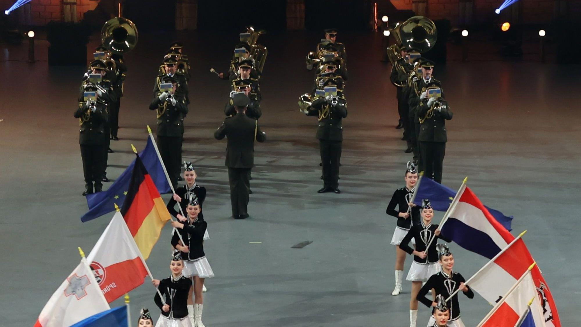 Fahnenträger der beteiligten Nationen vorne im Bild, dahinter ein Militärorchester