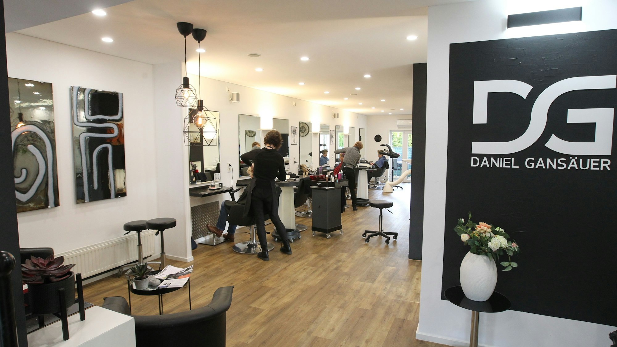 Die Räumlichkeiten des Friseursalons. Im Hintergrund sind Mitarbeiter, die Kunden betreuen.