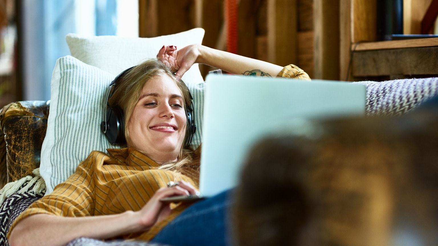 Eine Frau liegt auf dem Sofa, schaut auf einen Laptop und freut sich.