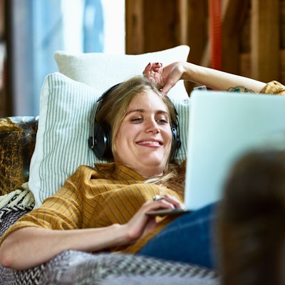 Eine Frau liegt auf dem Sofa, schaut auf einen Laptop und freut sich.
