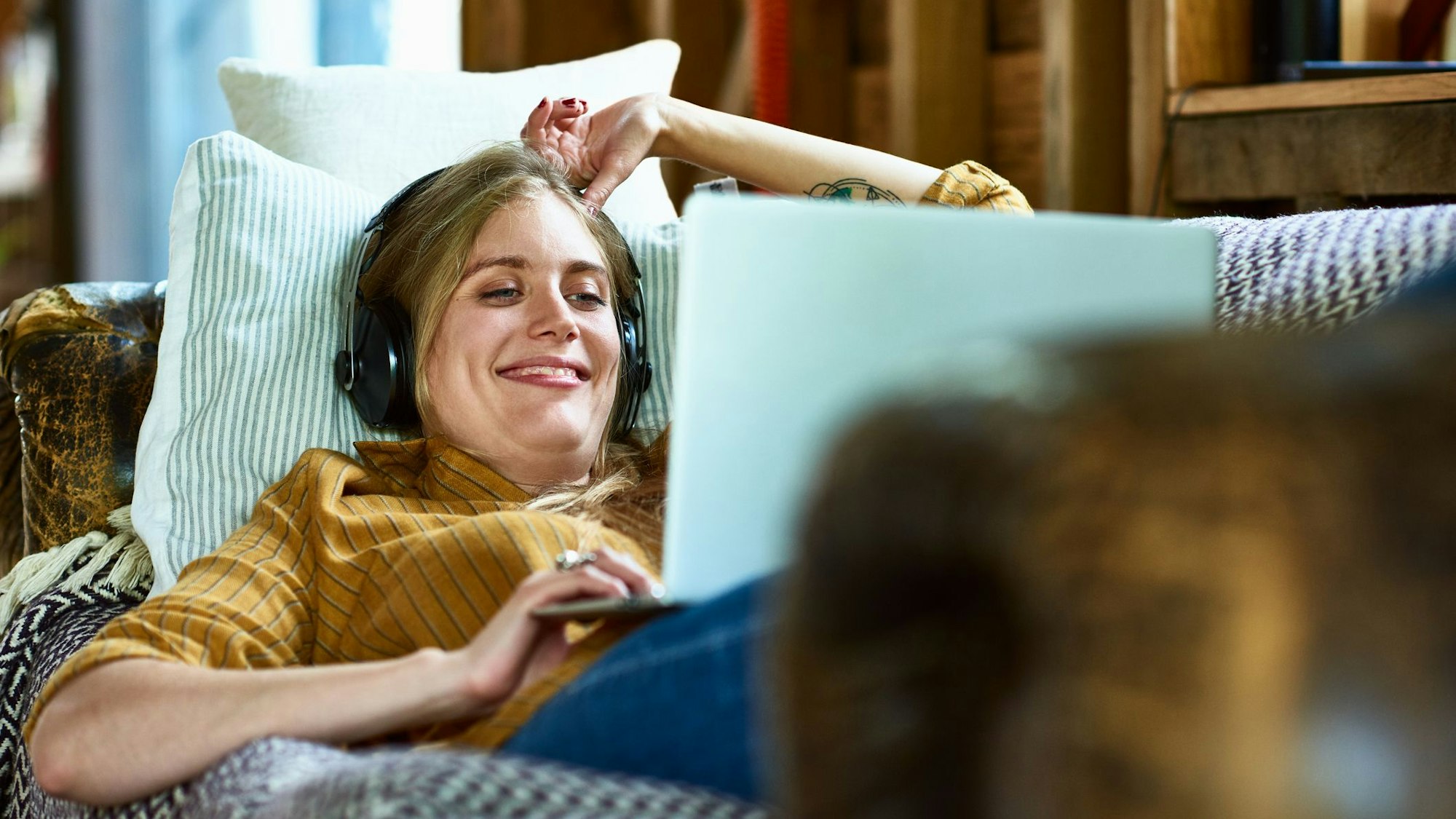 Eine Frau liegt auf dem Sofa, schaut auf einen Laptop und freut sich.
