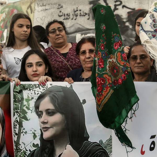 Kurdische Frauen schwenken bei einer Demonstration Kopftücher, während sie Bilder von Mahasa Amini in die Höhe halten.