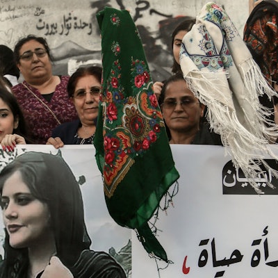 Kurdische Frauen schwenken bei einer Demonstration Kopftücher, während sie Bilder von Mahasa Amini in die Höhe halten.