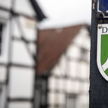 Ein Nordrhein-Westfälisches Denkmal-Schild mit der Aufschrift «Denkmal» ist am Balken eines Fachwerkhauses befestigt.
