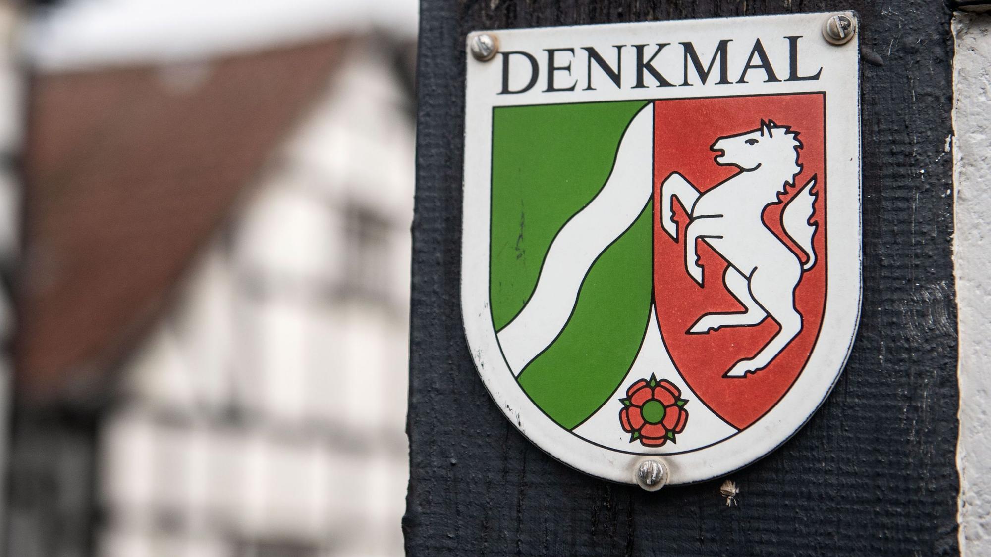 Ein Nordrhein-Westfälisches Denkmal-Schild mit der Aufschrift «Denkmal» ist am Balken eines Fachwerkhauses befestigt.