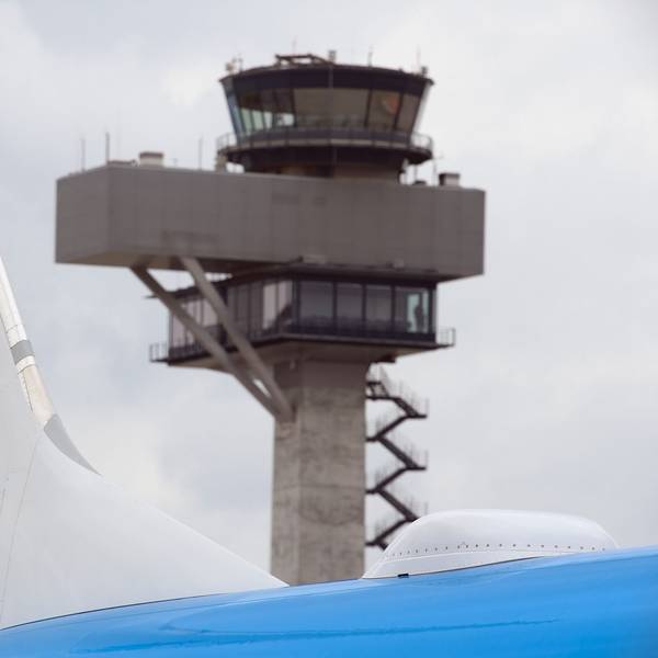 Eine Boeing 737 der niederländischen Fluggesellschaft KLM steht auf einem Rollfeld. Im Hintergrund ist ein Flughafen-Tower zu sehen.