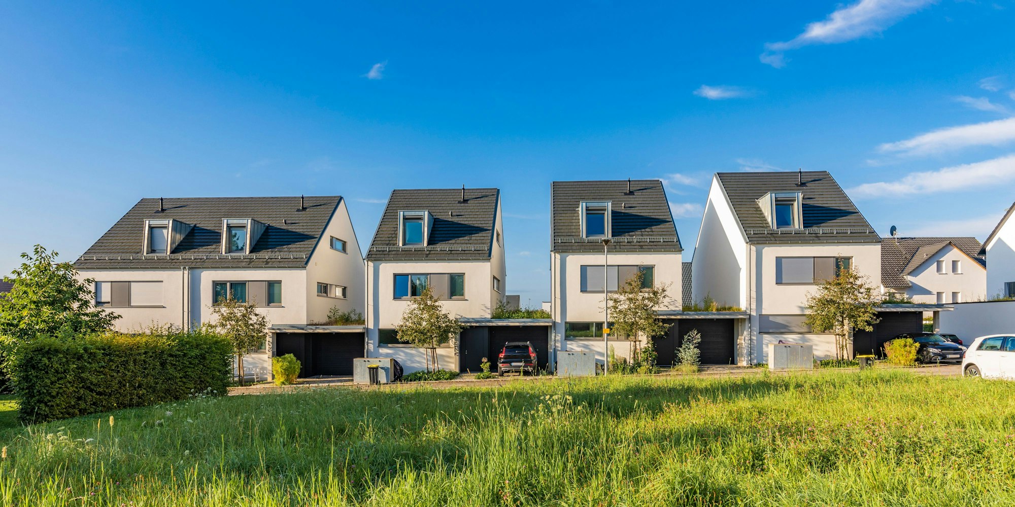 Vier Häuser stehen am Rand einer Wiese und von Garagen.