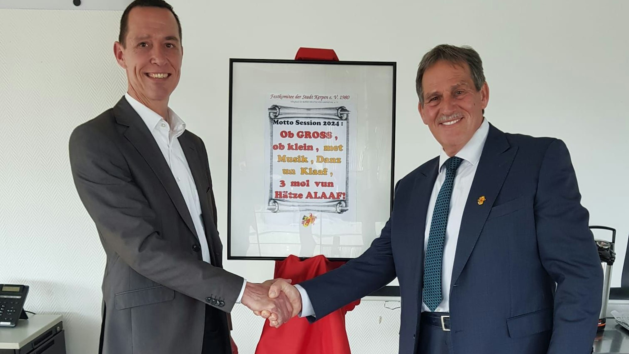 Das Foto zeigt Kerpens Bürgermeister Dieter Spürck und den Karnevalisten Jürgen Mein mit dem neuen Sessionsmotto.