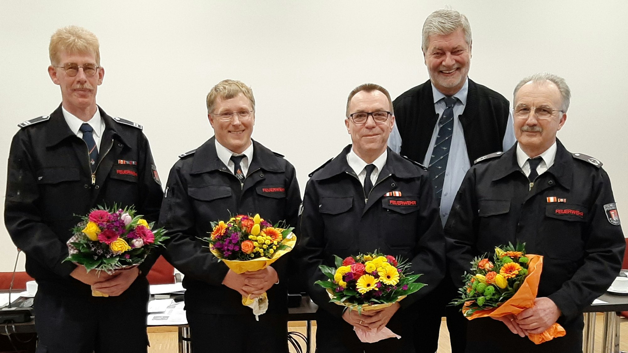 Neue und alte Wehrführung mit Blumensträußen und Bürgermeister Hilko Redenius im Ratssaal.