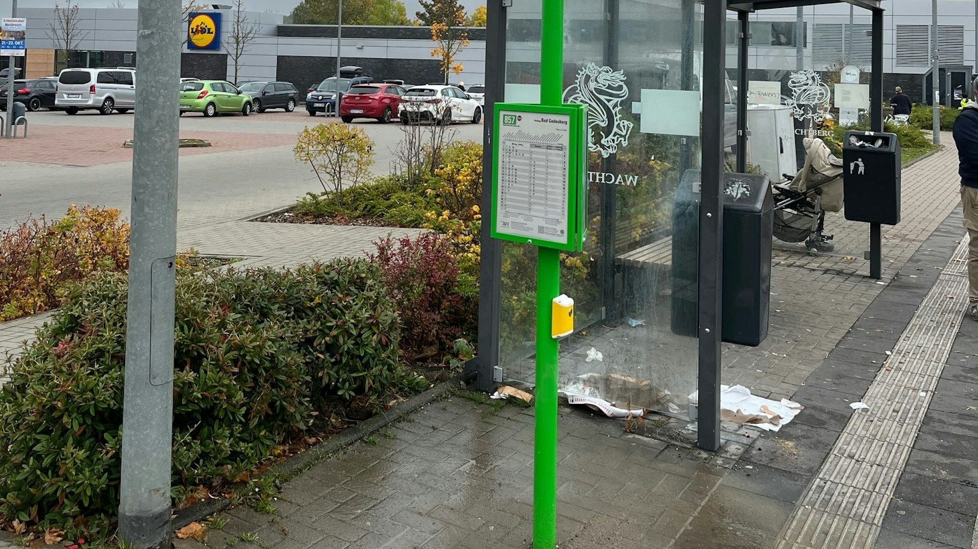 Eine Bushaltestelle steht ein grüner Mast, an dem ein gelbes Kästchen befestigt ist.