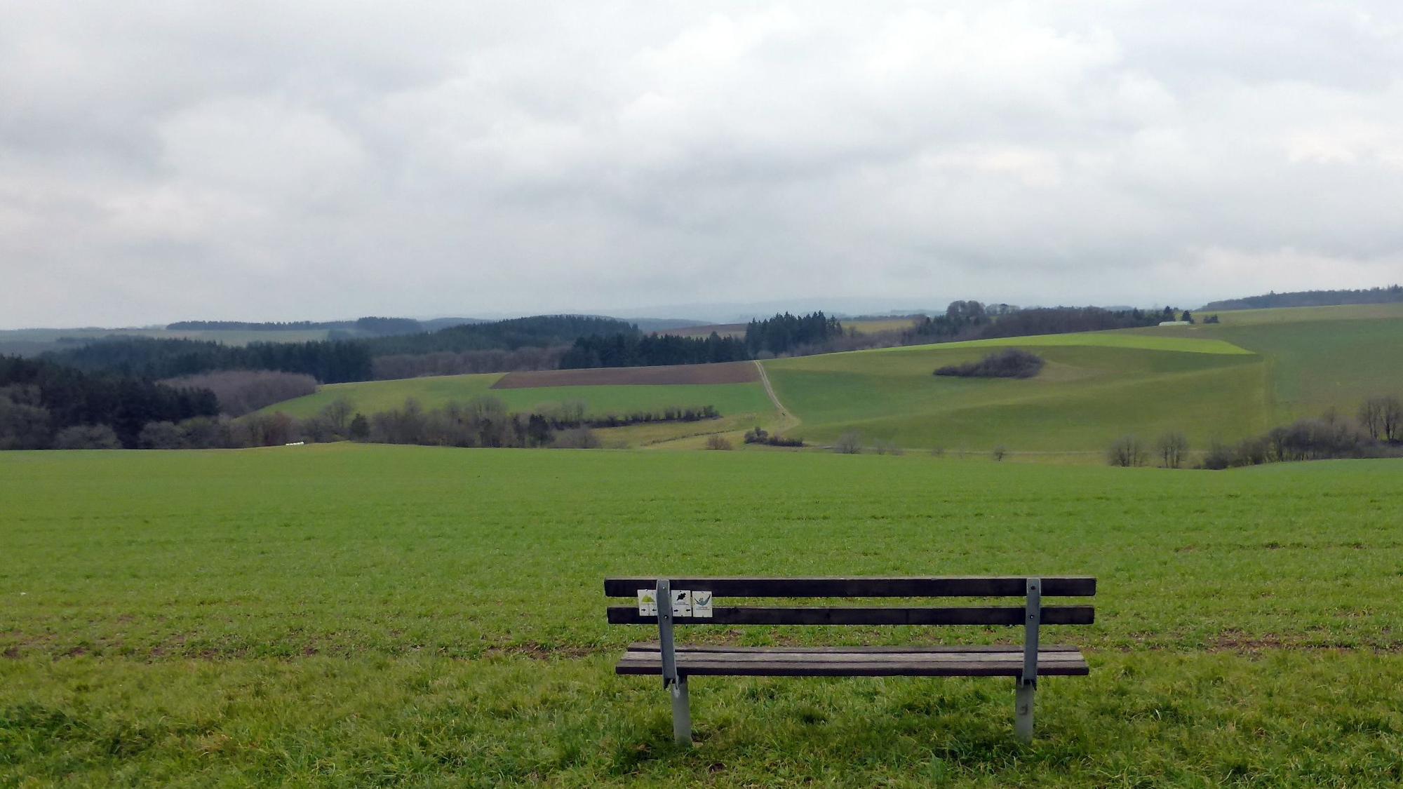 Eine Bank steht vor einem weiten Ausblick ins Tal