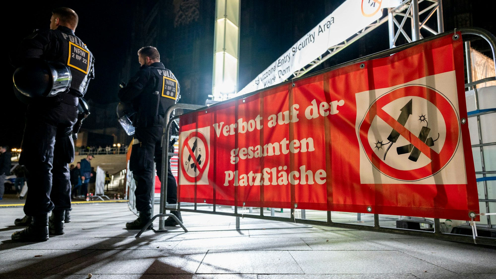 Polizisten stehen in der Nacht vor einem Feuerwerks-Verbotsschild.