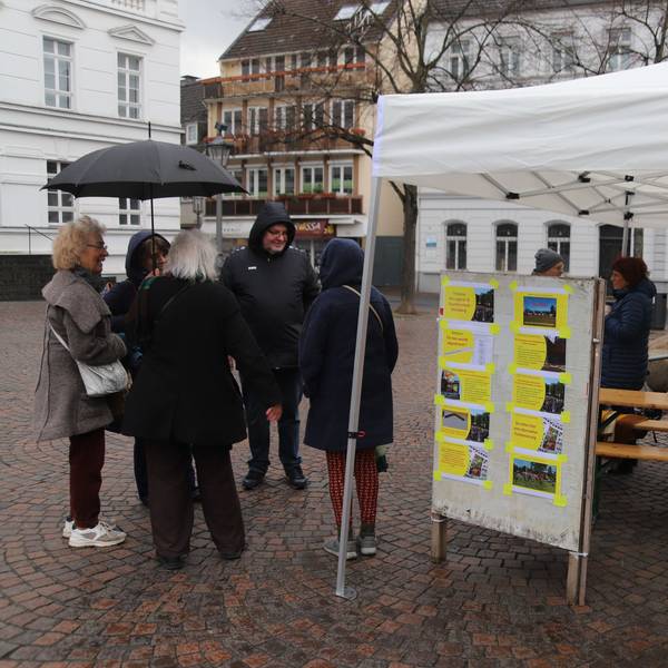 Blick auf das weiße Infostand-Zelt. Einige Leute stehen auf dem Platz davor.