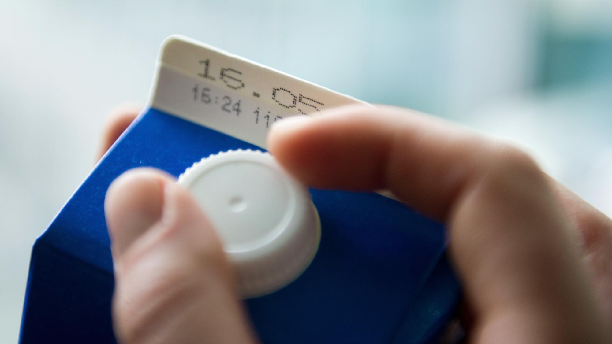 Eine Hand öffnet eine Tüte Milch, auf der eine Mindesthaltbarkeitsdatum steht