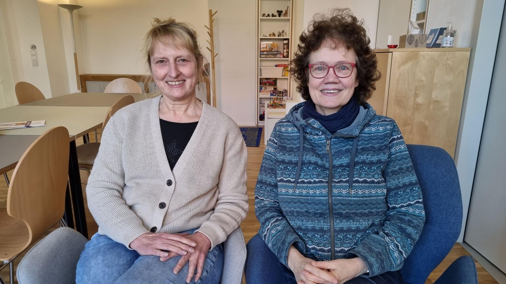 Ute Fingaß und Claudia Schrimpf sitzen auf zwei Sesseln in der Geschäftsstelle von „Frauen helfen Frauen“ in Köln und gucken in die Kamera.