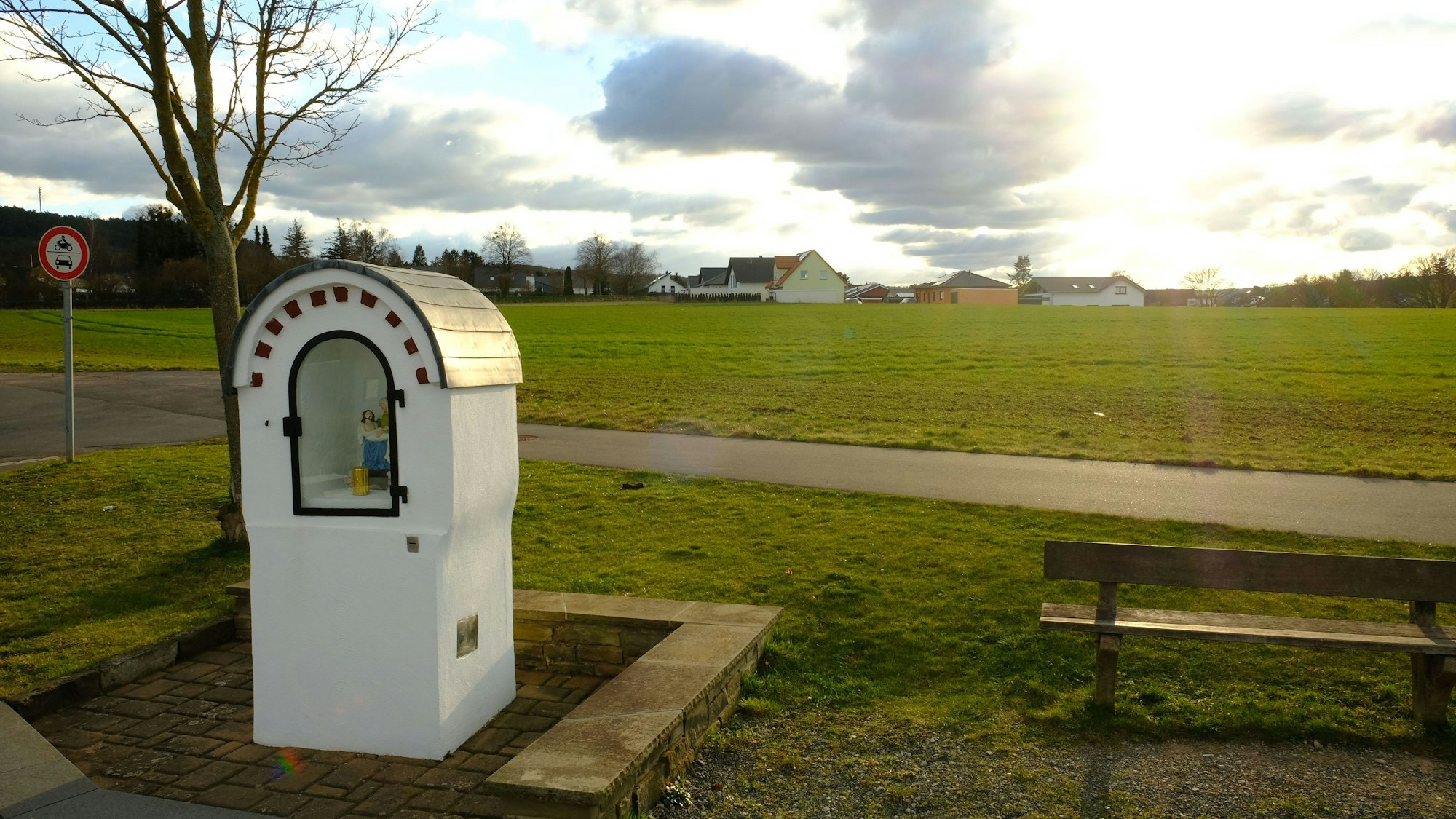 Hinter einem Heiligenhäuschen liegt ein Acker.