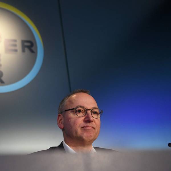 Werner Baumann sitzt in Leverkusen vor dem Bayer-Logo.