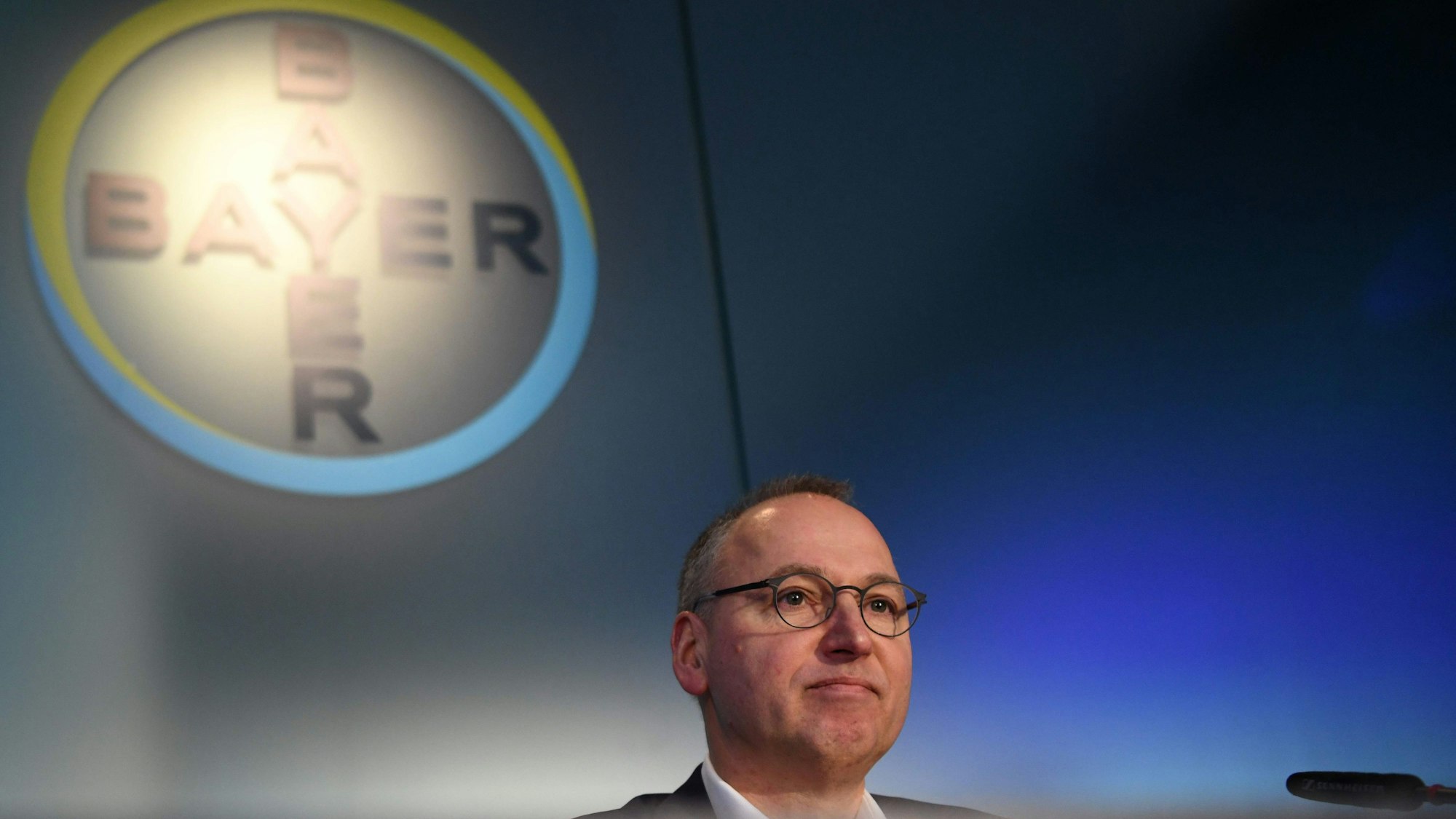 Werner Baumann sitzt in Leverkusen vor dem Bayer-Logo.