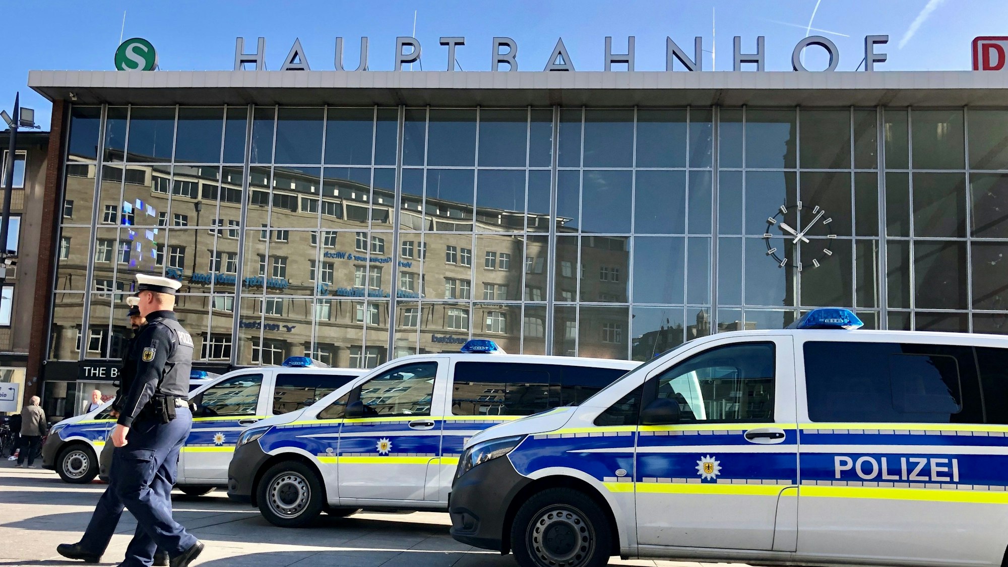 Drei Polizeiwagen stehen vor dem Kölner Hauptbahnhof. Zwei Polizisten stehen daneben.