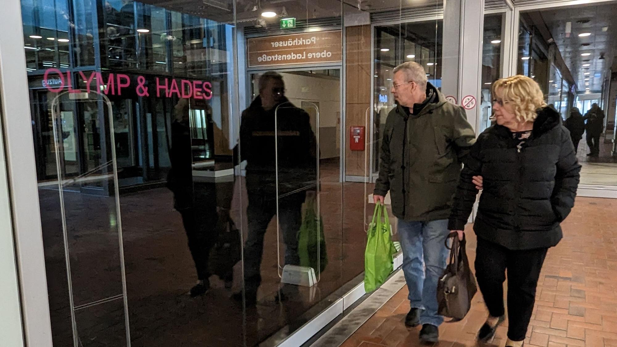 Das Foto zeigt zwei Passanten vor dem leerstehenden Ladenlokal des Textilhändlers Olymp & Hades.