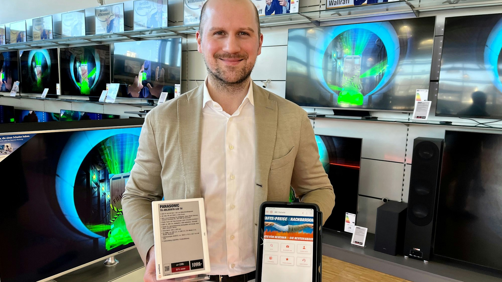 Alexander Wallraff hält ein digitales Preisschild und ein iPad in der Hand.